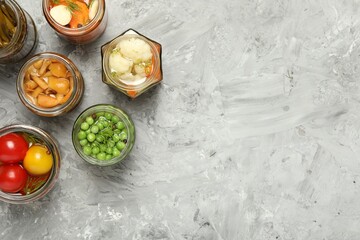Different pickled products in jars on grey table, flat lay. Space for text