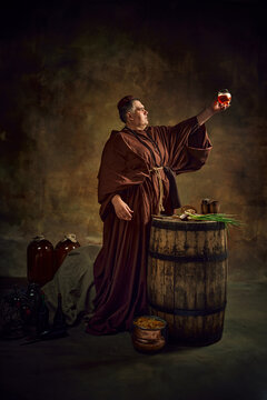 Dedication to abbey brewing through the ages. Medieval monk raising glass with freshly brewed ale, beer against stage background. Concept of comparison of eras, history, brewery, traditions