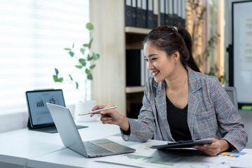 A woman is sitting at a desk with a laptop and a tablet