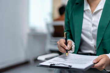 A woman in a green jacket is writing on a piece of paper