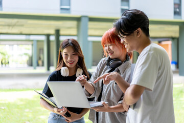 Three young people are standing in a grassy area, looking at a laptop