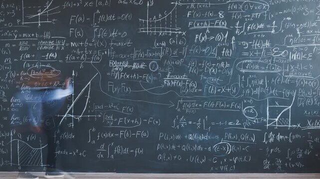 Time lapse of smart little boy writing maths formulas on chalkboard wall focused on calculation in classroom. Academic education and childhood concept.