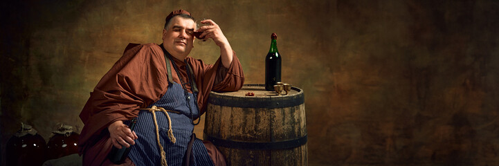 Hangover. Medieval man, monk in traditional attire leaning glass with beverage to head, leaning on...