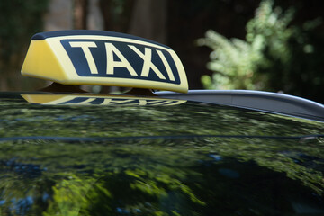A yellow and black taxi sign is on the roof of a car