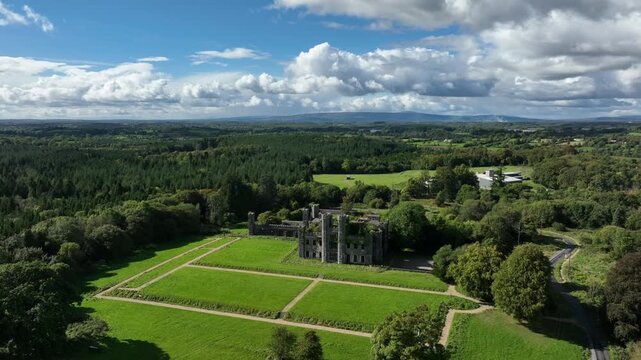 Castle Saunderson, County Cavan, Ireland, September 2022. Drone orbits clockwise in a wide aerial view of Gothic Revival Castle surrounded by lush green forest with the Finn River in the background.