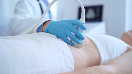 Doctor man wearing a blue medical gloves using an ultrasound equipment on a female patient lying down in clinic cabinet, close up view. Medicine concept