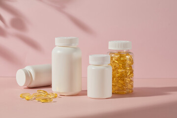 Pink background features some white blank label bottle of medicine and a fish oil supplement bottle, flat lay yellow capsules. Photo of front angle, copy space for adding text
