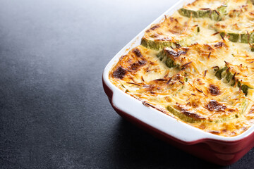Casserole with cheese and gratin zucchini on black slate background. Copy space