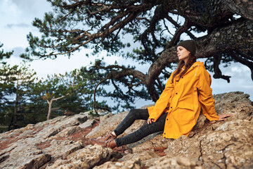 A woman in a yellow raincoat sitting on a rock in front of a tree during a nature retreat journey