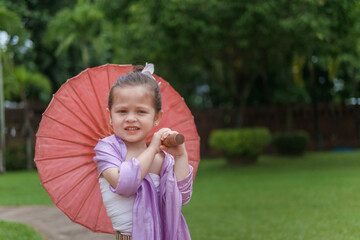 A young girl is holding a red umbrella and smiling. Concept of joy and playfulness, as the girl is dressed in a purple outfit and he is enjoying herself