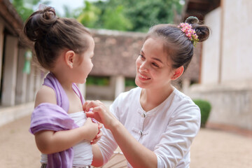 A woman is sitting with a child and is putting a purple scarf around the child's neck. The woman is smiling and the child is smiling as well. Scene is happy and loving