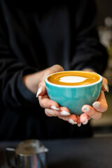 person holds a teal cup with a creamy latte, featuring intricate latte art. The focus is on the cup and beverage, suggesting a cozy, warm atmosphere. Ideal for coffee, beverage, and lifestyle themes.