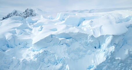 Massive blue ice wall glacier in Antarctica. Aerial close up fly over snow covered large iceberg surface, bright sunlight. Arctic frozen nature mountain beauty. Winter background. Discover South Pole