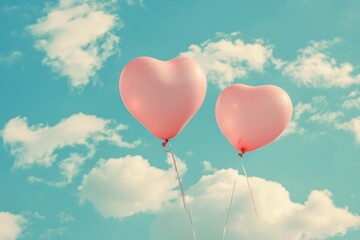 Obraz premium Two heart-shaped balloons floating in a clear blue sky with fluffy white clouds, symbolizing love and joy.