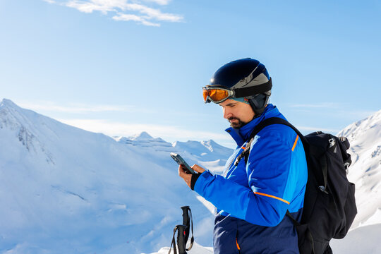 Young adult skier use smartphone make selfie navigate online map app winter alpine skiing resort. Male sporty person with backpack using mobile phone mountain Alps snow slope outdoors cold snowy day