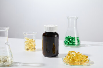 Black mockup bottle without label featured on white background with several glassware contain colorful vitamin capsule placed around. Front view, blank space for advertisement