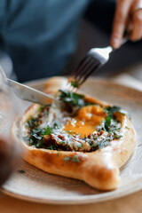 sweet girl in a blue dress is eating delicious khachapuri with juicy meat, fresh vegetables, fragrant herbs, and crispy dough on a beautiful white plate in a cozy nice restaurant