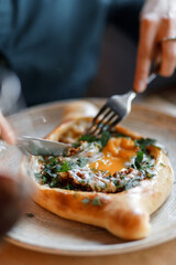 sweet girl in a blue dress is eating delicious khachapuri with juicy meat, fresh vegetables, fragrant herbs, and crispy dough on a beautiful white plate in a cozy nice restaurant