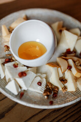 delicious cheese platter with juicy cheese, nuts, fresh red pomegranate, and yellow sauce on a beautiful white plate in a cozy nice restaurant