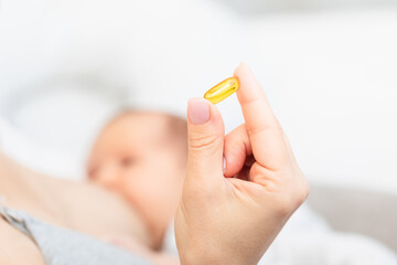 Hand Holding Yellow Pill with Breastfeeding Baby in Background