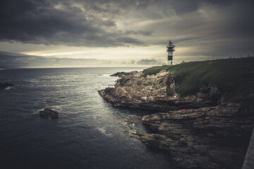 Fototapeta premium Night seascape with lighthouse in the dark night stormy nines. sunset background lighthouse Isla Pacha Ribadeo Galicia Spain. iconic old lighthouse on rocky island, coastal landscape with cliffs.