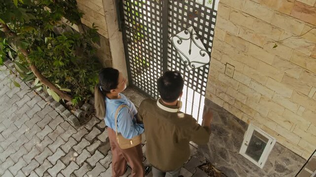 View from above of Asian couple ringing doorbell while visiting friends outdoors
