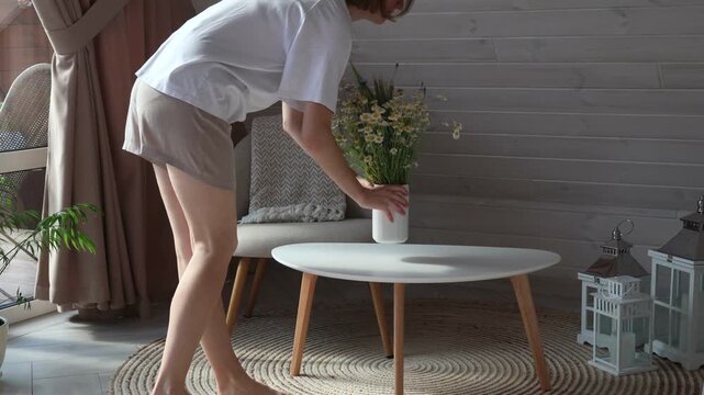 Woman takes a vase with flowers from the table.