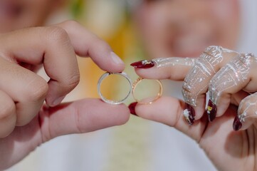 Detailed photo of two gold and silver wedding rings held by the hands of the bride and groom with...