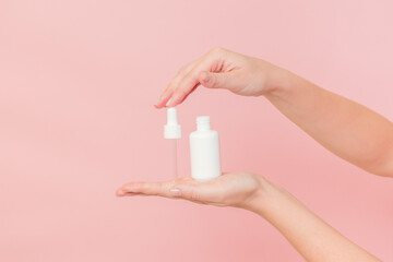 White tube with pipette with serum lotion or essential oil (hyaluronic acid and collagen) in hands on pink background. Skin care cosmetics concept, beauty flyer