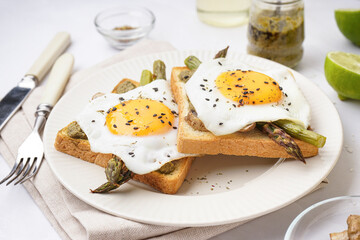 Delicious sandwiches with fried eggs and asparagus on light background