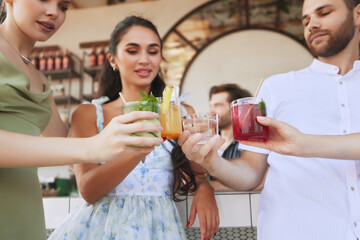 Friends , men and women gathering at trendy bar, toasting with vibrant cocktails and sharing good time together. Concept of friendship, party, leisure, celebration, relaxation