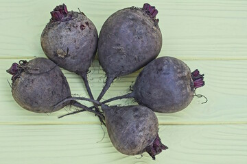 five gray raw beets lie on a yellow wooden table