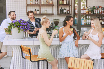 Group of friends,men and women relaxing with cocktails at outdoor bar, engaging in lively conversation. Cheering moment. Concept of friendship, party, leisure, celebration, relaxation