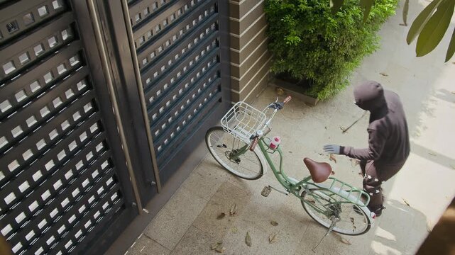 View from above on thief in black clothes stealing bicycle near gate at daylight
