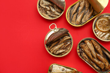 Opened tin cans with different fish on red background