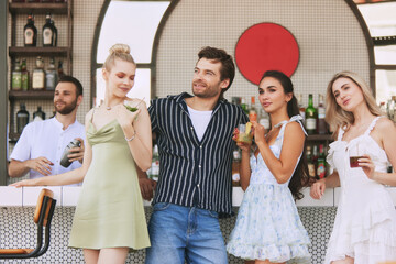 Friends, men and women enjoying cocktails a stylish bar, posing for memorable moment together. Cheerful evening. Concept of friendship, party, leisure, celebration, relaxation