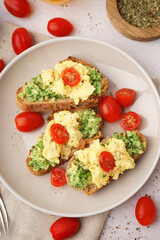 Plate with tasty scrambled eggs sandwiches and vegetables on light background