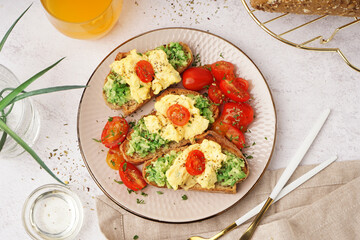 Plate with tasty scrambled eggs sandwich and vegetables on light background