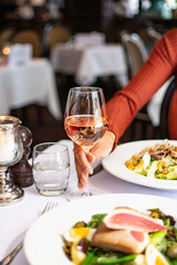 A hand holding a glass of rosé in a restaurants with salads