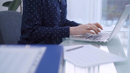 A female accountant or businesswoman with blue dotted blousy is typing on laptop computer on glass...