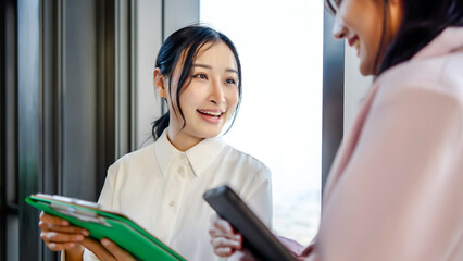 Obraz premium Young asian business woman hold the paper clipboard and digital tablet to show or consult or discussion to the colleague in the office in evening, Talk about investments, finances, profits and losses