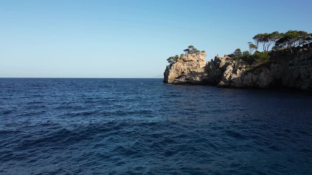 Drone flying towards tall rocky cliffs along the shore of Cala Murta, Mallorca