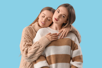 Young lesbian couple in warm sweaters hugging on blue background