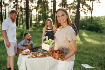 Strawberry in hands of woman. Group of friends are having picnic on the field with food in eco boxes