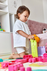 cute baby girl playing with colorful toys bricks at home