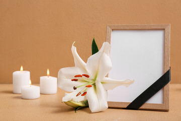 White lily, blank funeral photo frame and candles on beige background