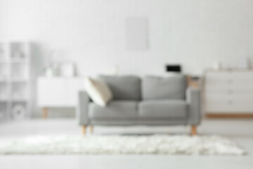 Interior of light living room with grey sofa, chest of drawers and carpet, blurred view