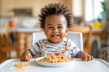 Fotobehang Funny portrait of a baby eating spaghetti and smiling. The baby has a face full of tomato sauce. © EJManzaneque