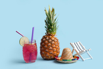 Fresh pineapple with glass of cocktail, sombrero hat and deck chair on blue background