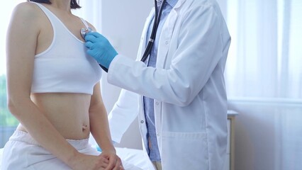Obraz premium Doctor and patient. Physician wearing blue medical gloves is using stethoscope examining woman lungs in clinic. Medicine concept